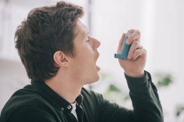 side view of handsome man using inhaler at home  clipart