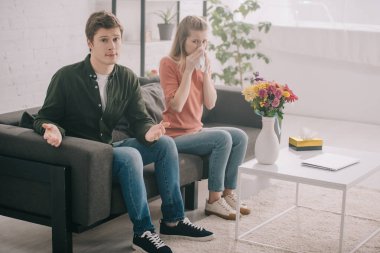 yakışıklı adam omuz silkme hareketi çiçekli vazo ve hapşırma sarışın kız polen alerjisi yakınındaki otururken gösterilen