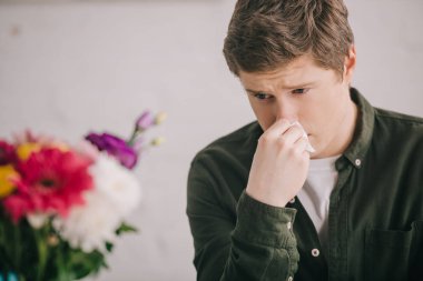 selective focus of sad man with pollen allergy looking at blooming flowers  clipart