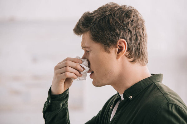 handsome man holding tissue and sneezing with closed eyes 