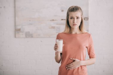 upset woman with lactose intolerance holding glass of milk  clipart