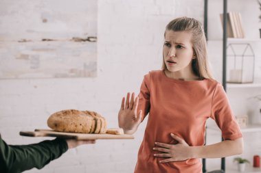 cropped view of man holding cutting board with bread near upset blonde woman with gluten allergy  clipart