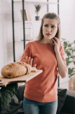 kesme tahtası ile ekmek gluten alerjisi olan üzgün sarışın kadın yakınındaki tutan adamın kırpılmış görünümü 