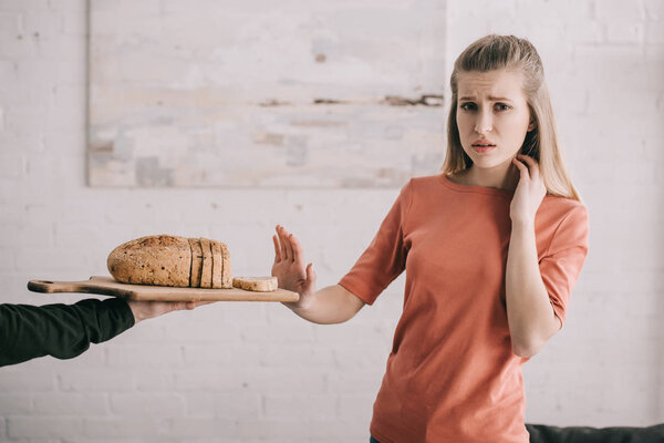 cropped view of man holding cutting board with sliced bread near sad blonde woman with gluten allergy 