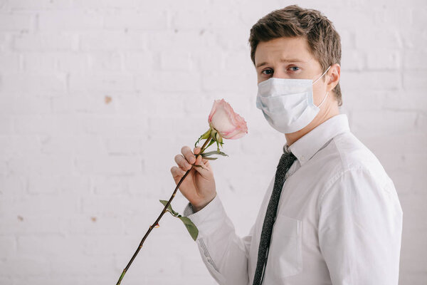 man in medical mask holding rose and looking at camera 