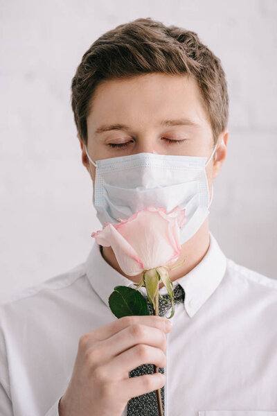 man with pollen allergy in medical mask smelling rose with closed eyes