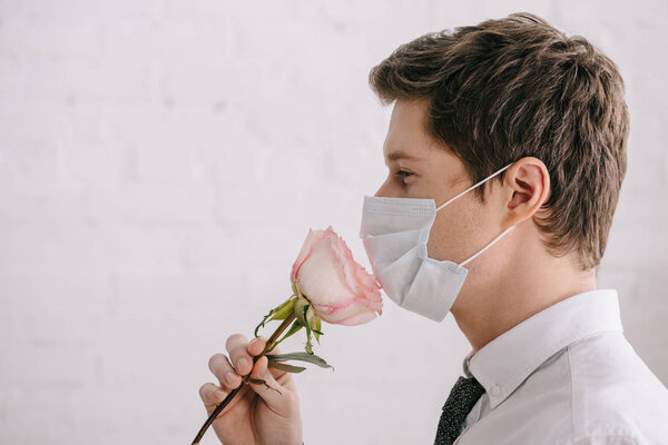 side view of man with pollen allergy in medical mask smelling rose 