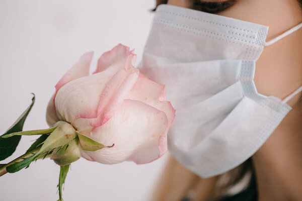 cropped view of woman in medical mask smelling rose 