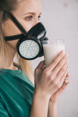 blonde woman in respiratory mask smelling milk while holding glass clipart