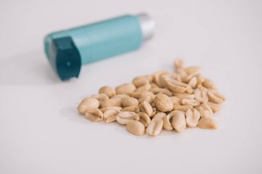 selective focus of tasty nutritious peanuts near blue inhaler on grey  clipart