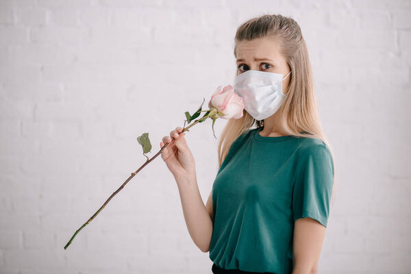 scared woman with pollen allergy wearing medical mask and smelling rose 
