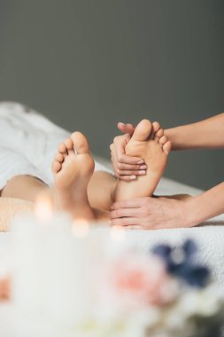 partial view of masseur doing foot massage to adult woman in spa