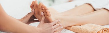 panoramic shot of masseur doing foot massage to adult woman in spa clipart
