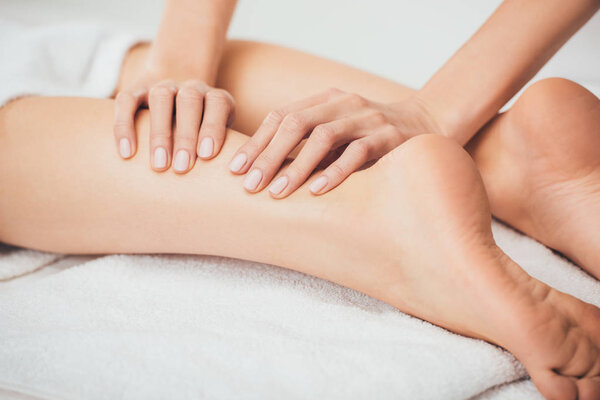 partial view of masseur doing foot massage to adult woman in spa