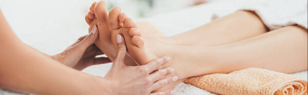 panoramic shot of masseur doing foot massage to adult woman in spa