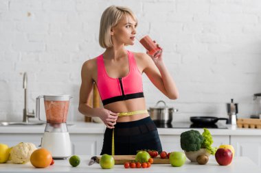Mutfakta sarışın kız spor içme Smoothie ve Holding ölçme bandı 