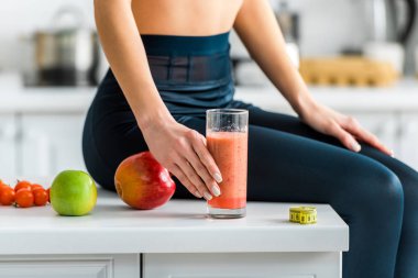 elma yakın mutfakta otururken kız Smoothie cam tutan kırpılmış görünümü