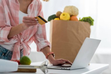 bakkal ile kağıt çantası yakın laptop kullanırken genç kadın tutan kredi kartı kırpılmış görünümü 