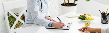 panoramic shot of nutritionist writing diagnosis near patient  clipart