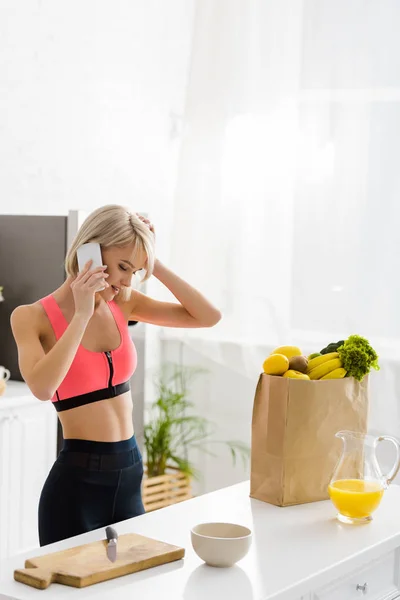 Blondes Mädchen Sportkleidung Spricht Auf Smartphone Neben Papiertüte Mit Lebensmitteln — Stockfoto