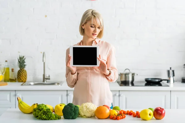 キッチンの食べ物の近くに空白の画面でデジタルタブレットを保持しているブロンドの妊娠女性 — ストック写真