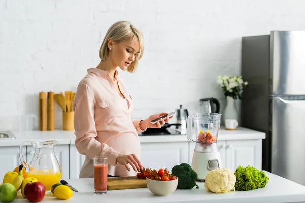 Těhotná Blondýnka Která Drží Smartphone Kuchyni Ovocem Zeleninou — Stock fotografie