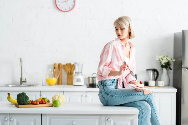 Chica Rubia Sosteniendo Tenedor Platillo Con Pastel Dulce Mirando Frutas —  Fotos de Stock