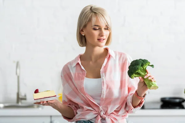 Blonde Girl Looking Organic Broccoli While Holding Saucer Sweet Cake — Stock Photo, Image