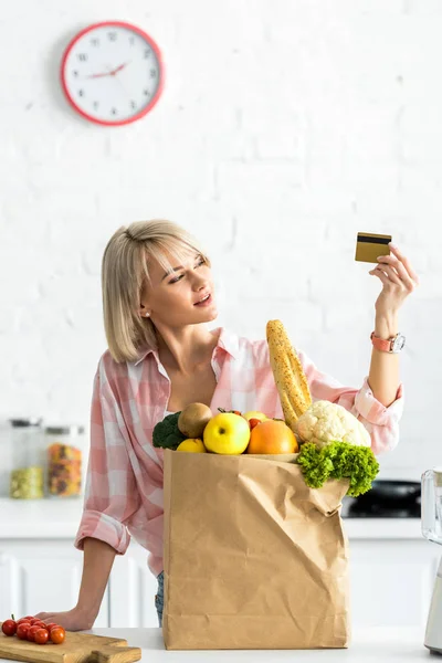 Atractiva Chica Sosteniendo Tarjeta Crédito Cerca Bolsa Papel Con Comestibles —  Fotos de Stock