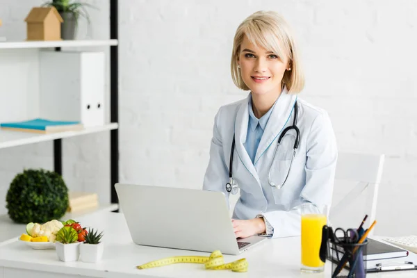 Vrolijke Blonde Voedingsdeskundige Zittend Buurt Van Laptop Glas Verse Jus — Stockfoto