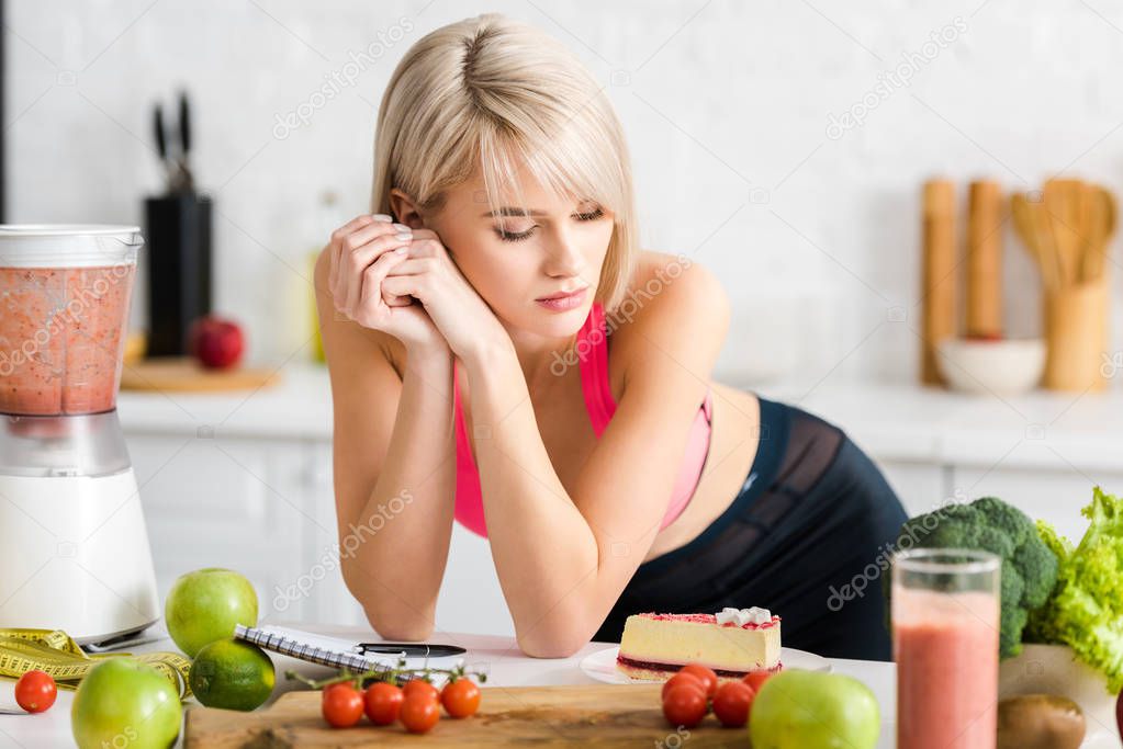 attractive blonde girl in sportswear looking at cake in kitchen 