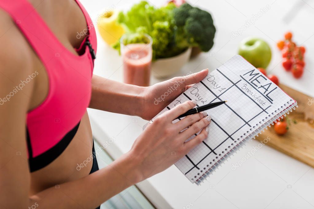 cropped view of sportswoman holding notebook with meal lettering in kitchen 