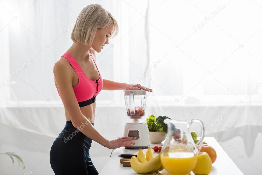 attractive blonde sportswoman preparing smoothie in blender 
