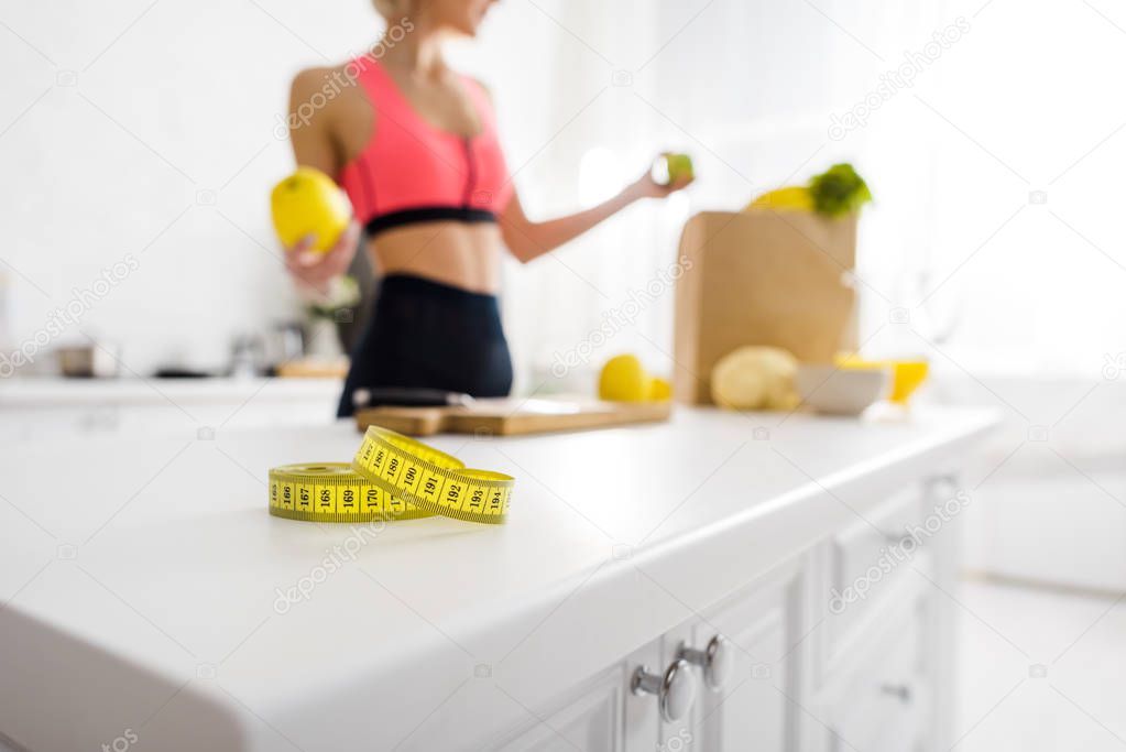 cropped view of woman holding apple near measuring tape in kitchen 