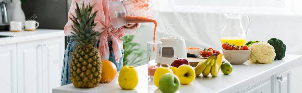 panoramic shot of young woman pouring tasty smoothie in glass  