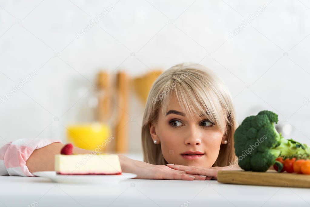 blonde girl looking at saucer with sweet cake near organic vegetables 