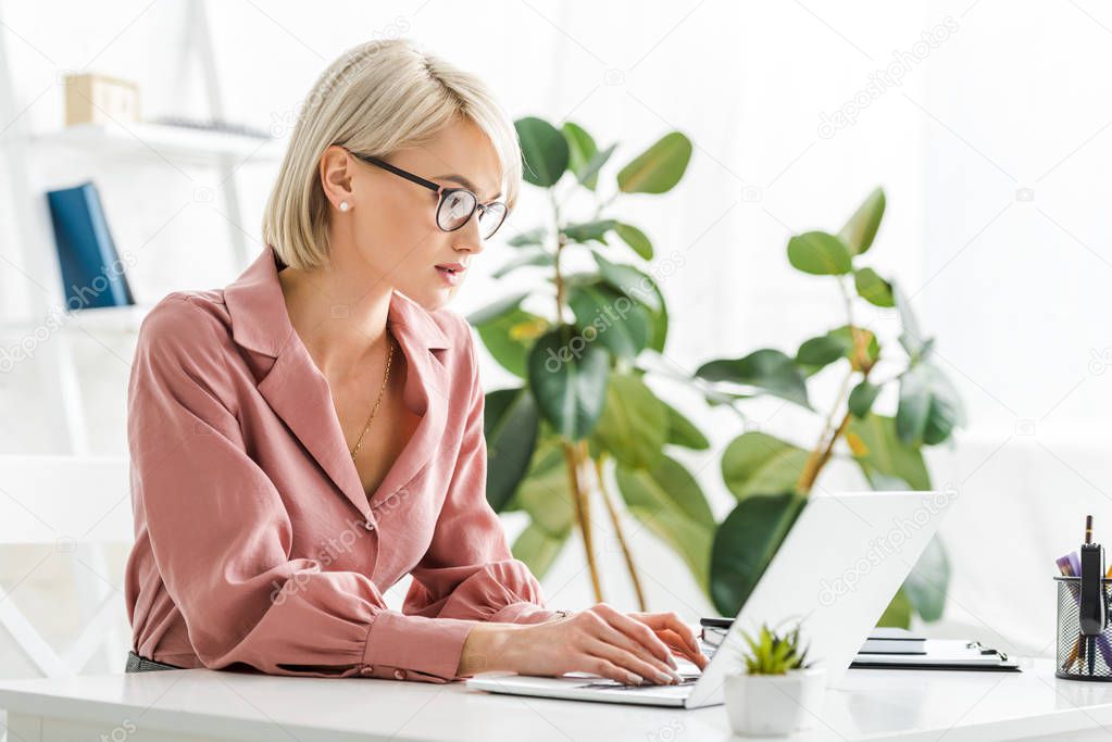 attractive young blonde freelancer in glasses typing on laptop 