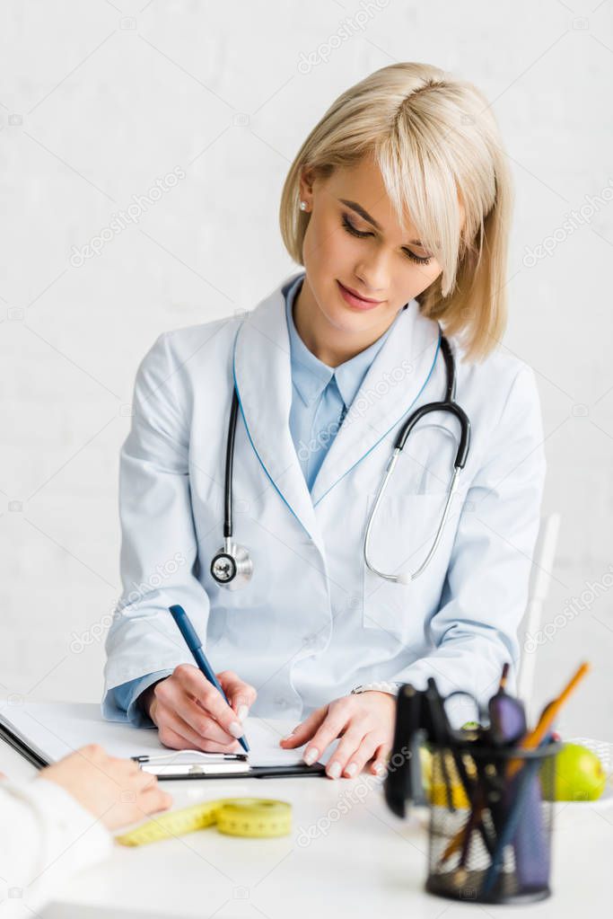 attractive blonde nutritionist writing diagnosis near patient 