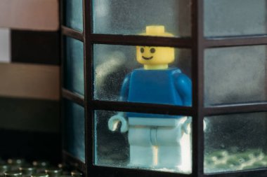 KYIV, UKRAINE - MARCH 15, 2019: lego figurine with smiley face looking through window in block house clipart