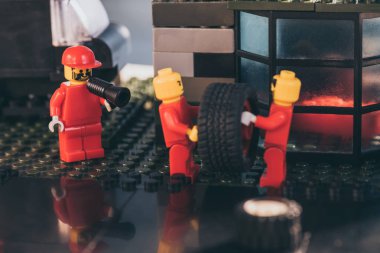 KYIV, UKRAINE - MARCH 15, 2019: lego minifigures in red carrying tire while other figurine shouting in mouthpiece at service station clipart