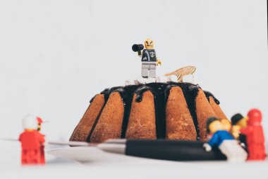 KYIV, UKRAINE - MARCH 15, 2019: lego character with mouthpiece standing on cake and shouting at other figurines on white clipart