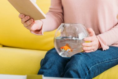 Dizlerinin üzerinde balık kase ile otururken kadın tutan kitap kısmi görünümü