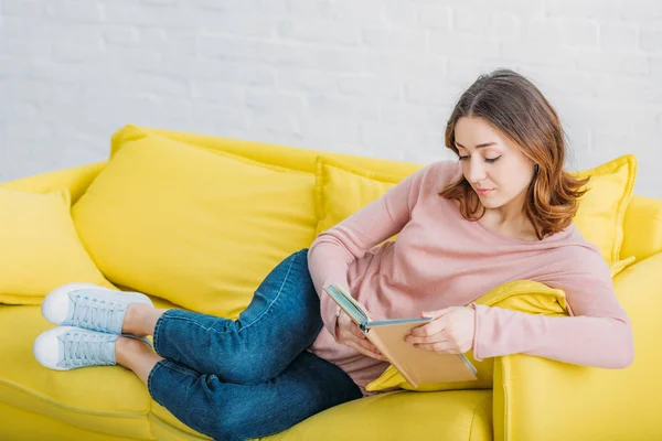 Bela Jovem Mulher Ler Livro Enquanto Descansa Sofá Amarelo Casa — Fotografia de Stock