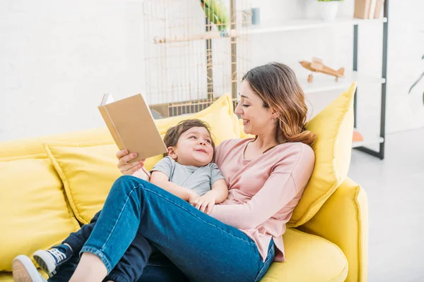 Vrolijke Moeder Met Boek Schattige Lachende Jongen Rusten Gele Sofa — Stockfoto