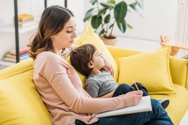 Attente Vrouw Schrijven Notebook Zittend Sofa Met Schattige Zoon — Stockfoto