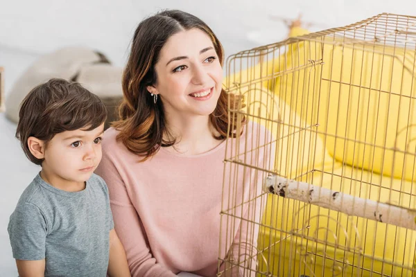 Feliz Madre Con Adorable Hijo Atento Mirando Pájaro Jaula Casa — Foto de Stock