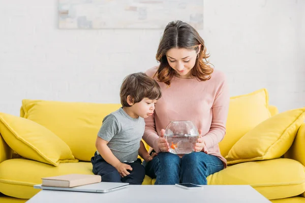 Aantrekkelijke Vrouw Holding Fishbowl Zittend Gele Sofa Met Schattige Zoon — Stockfoto