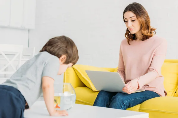 Mulher Bonita Usando Laptop Enquanto Filho Adorável Olhando Para Tigela — Fotografia de Stock