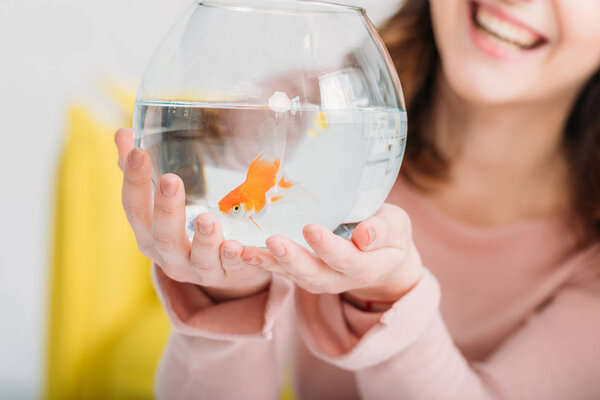 partial view of cheerful woman holding fish bowl with bright gold fish