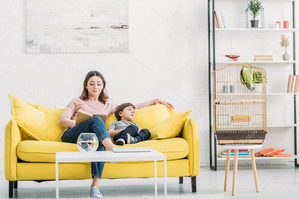 attractive woman with adorable son resting on yellow sofa in spacious living room